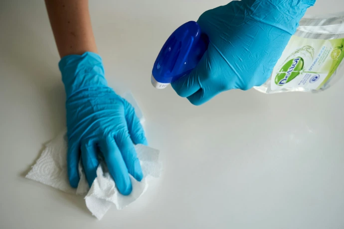 A person in blue gloves wiping a white surface with a paper towel